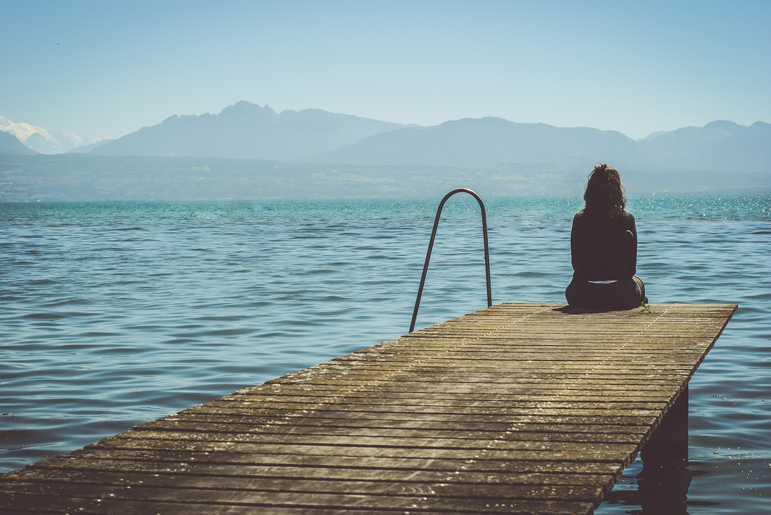 Picture of woman sitting alone on a pier. 